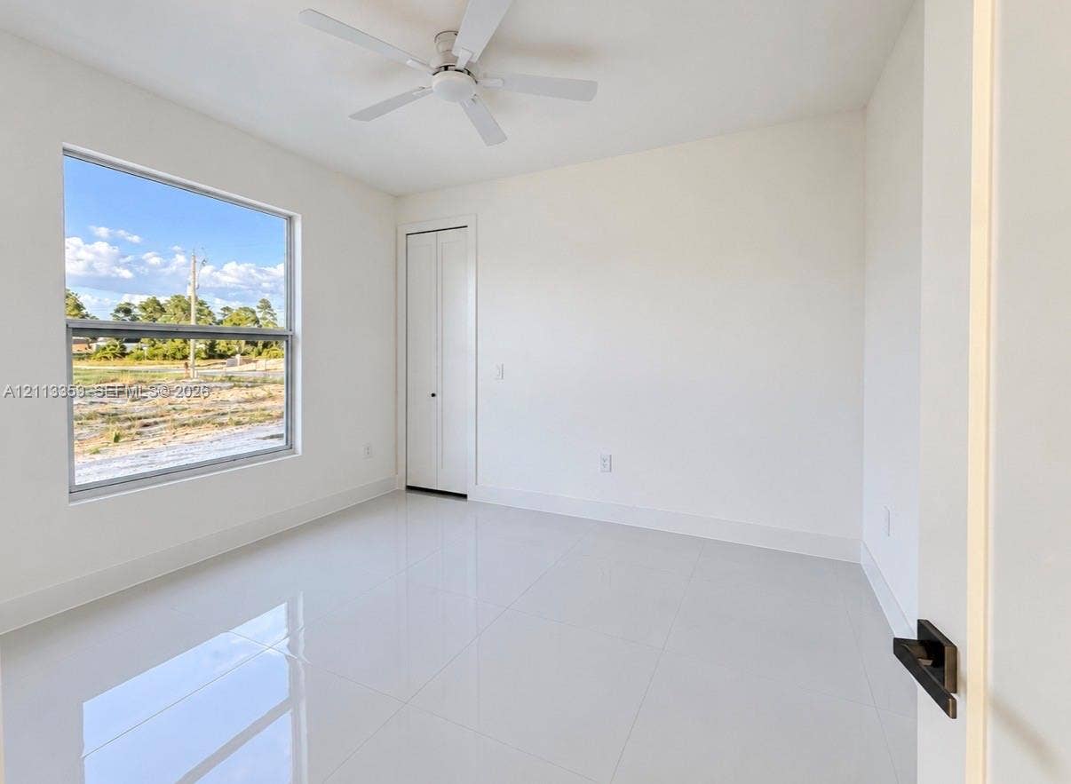 Interior space featuring large-format tile flooring, crisp white walls, a ceiling fan, and a bi-fold closet door