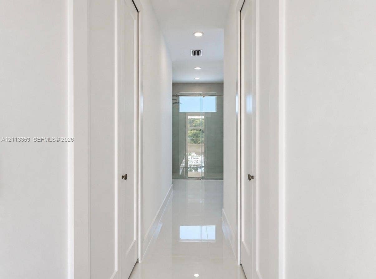 Hallway featuring high-gloss tile flooring, recessed ceiling lighting, and dual floor-to-ceiling closets with paneled doors