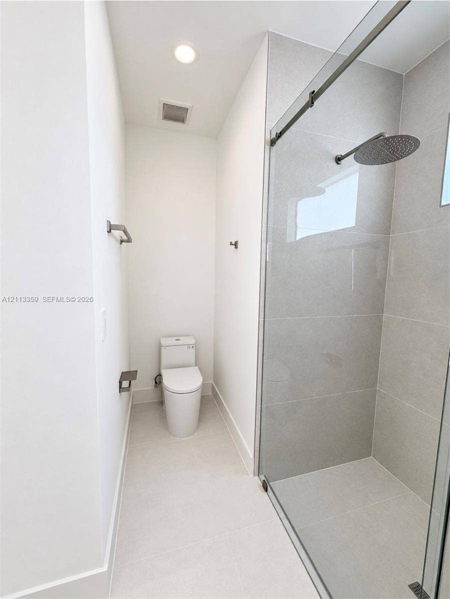 Walk-in shower featuring large-format ceramic wall tile, a glass sliding enclosure, and a ceiling-mounted rainfall showerhead, complemented by a dual-flush elongated toilet