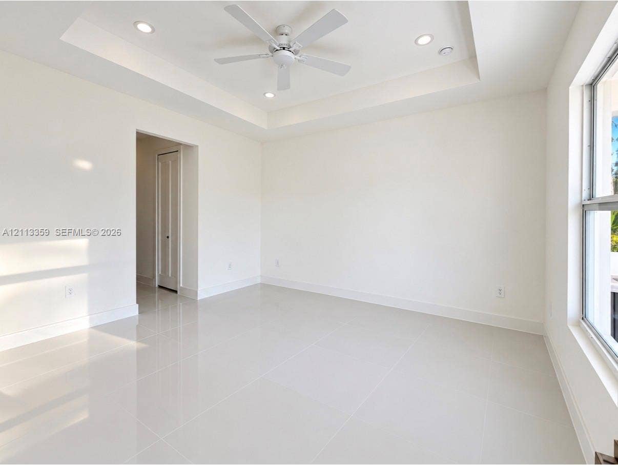 Tray ceiling with recessed lighting, white tile flooring, ceiling fan, and large windows
