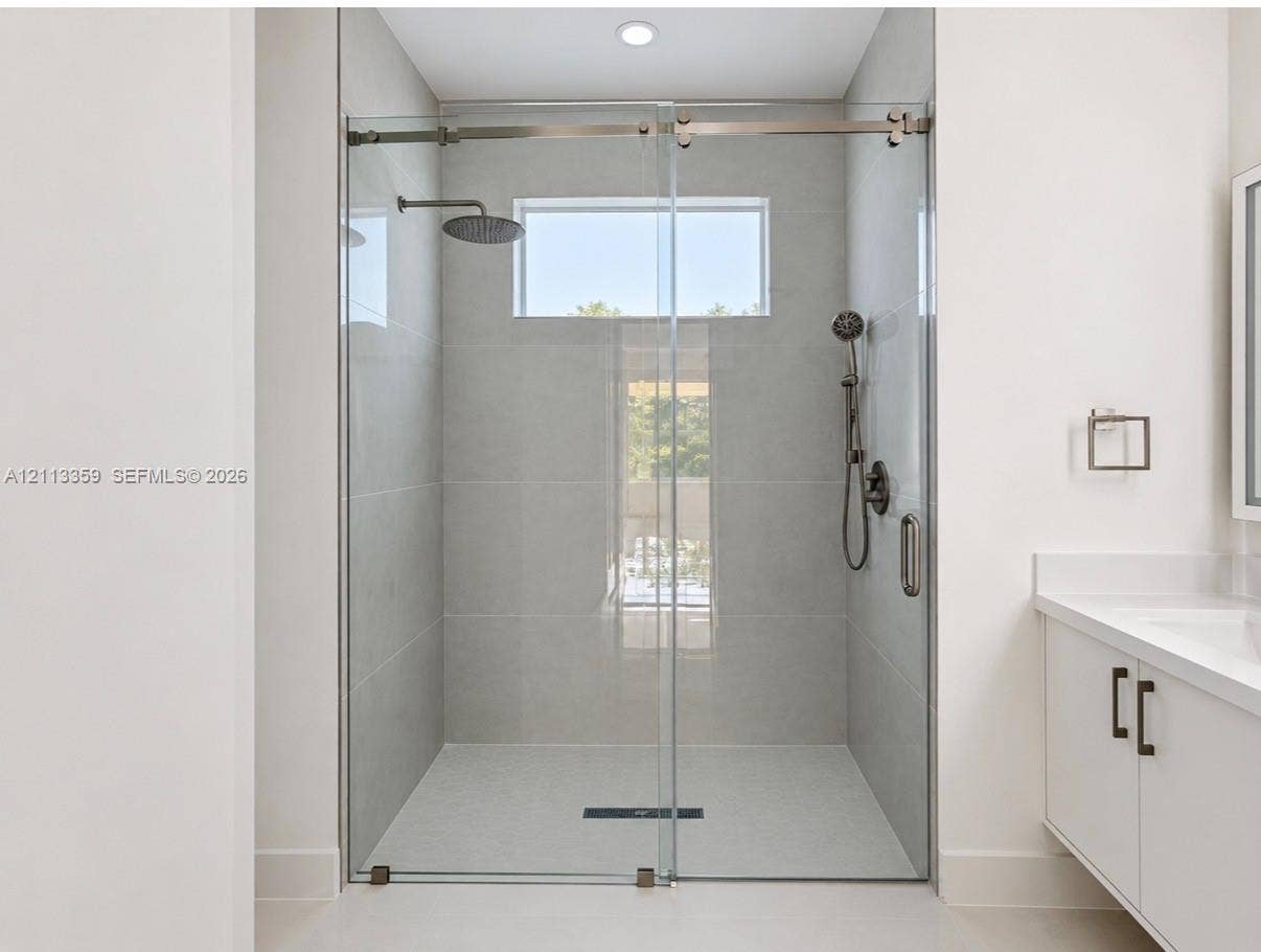 Walk-in shower featuring large-format tile surround, frameless glass sliding enclosure, rainfall showerhead, handheld sprayer, and transom window