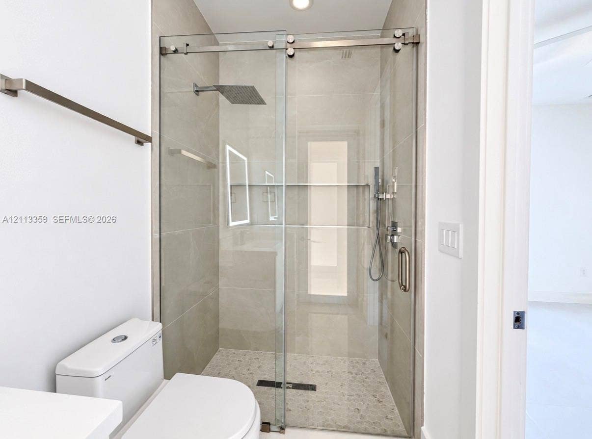 Walk-in shower featuring a frameless glass sliding door, large-format tile surround, rainfall shower head, integrated tiled shelving niche, and pebble-textured floor tiling