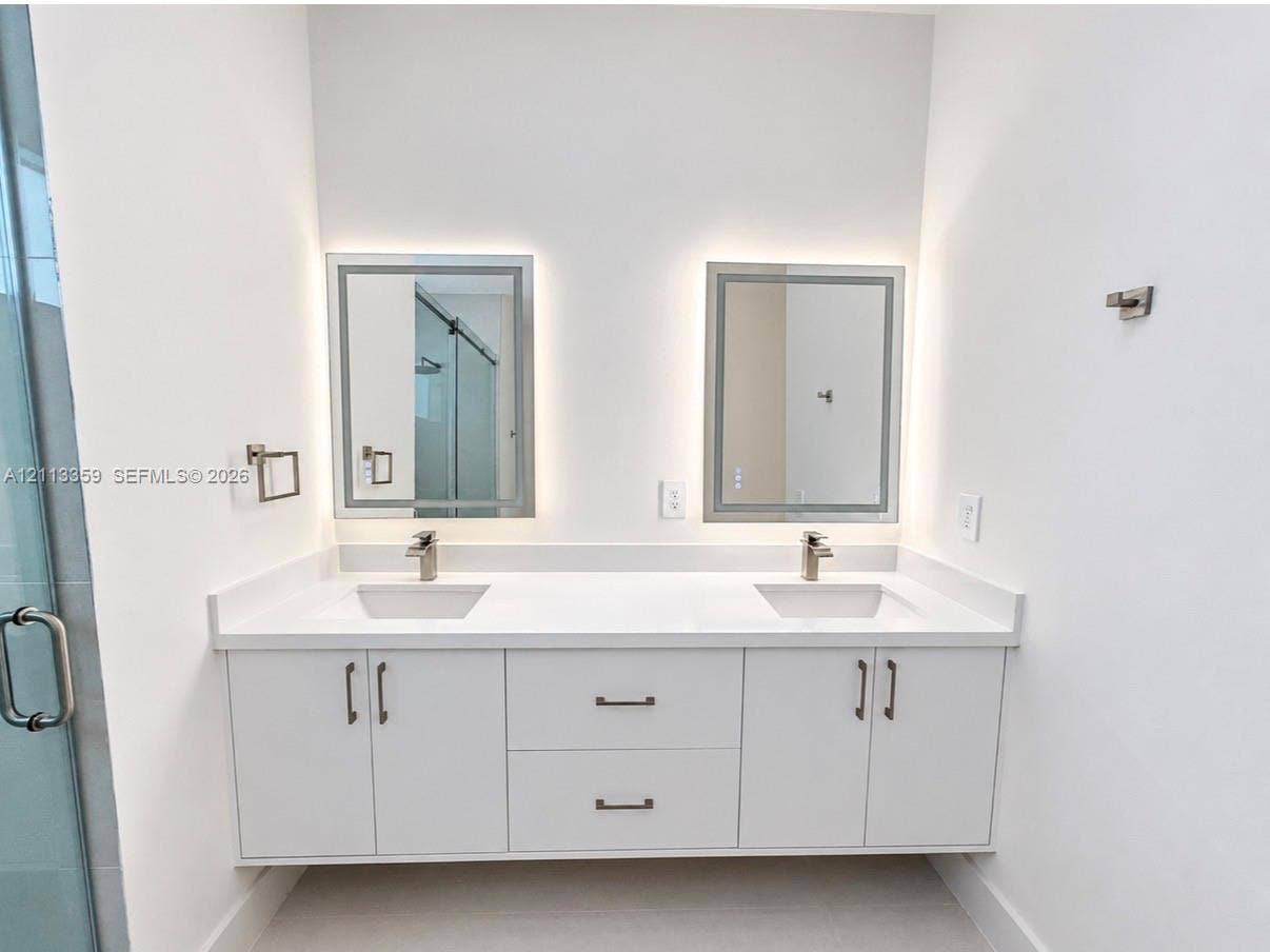 Floating double vanity featuring a white countertop with dual undermount sinks, satin-finish faucets, built-in lower cabinetry, and two rectangular LED-backlit mirrors