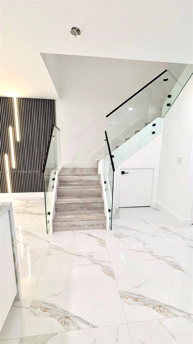 9395 Boca River Circle, Boca Raton, Boca Raton, FL 33434 Staircase featuring wood-finish treads, frameless glass railings with black hardware, and vertical slat accent wall paneling over large-format tile flooring