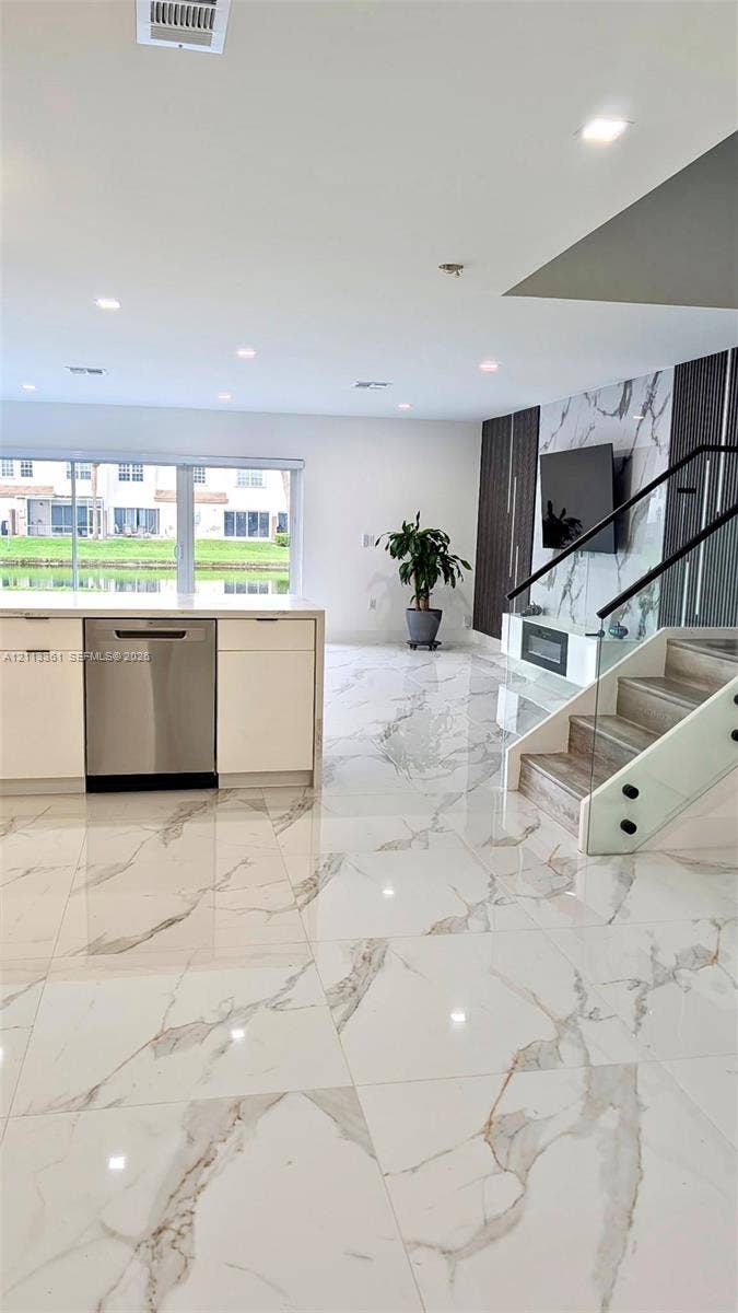 9395 Boca River Circle, Boca Raton, Boca Raton, FL 33434 Large-format stone flooring featuring a veined pattern, white flat-panel cabinetry, stainless steel dishwasher, glass-panel staircase railing, and built-in electric fireplace with vertical accent lighting