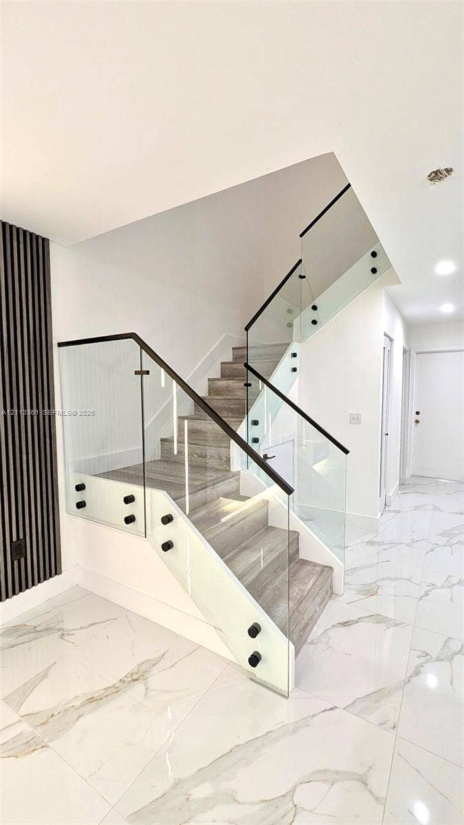9395 Boca River Circle, Boca Raton, Boca Raton, FL 33434 Large-format polished tile flooring, slat-wall accent paneling with integrated lighting, stone-finish fireplace surround, quartz-topped island with slat detailing, and glass-paneled staircase railing