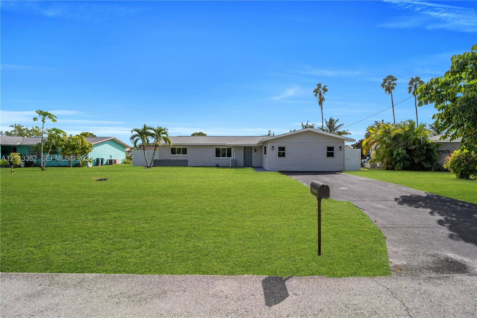 1206 NE 4th Terrace, Cape Coral, FL 33909 Single-story exterior featuring a neutral-toned facade, an attached driveway, and expansive lawn space