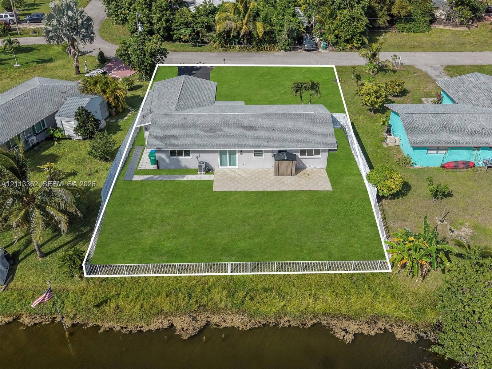 1206 NE 4th Terrace, Cape Coral, FL 33909 Single-story residence featuring a paved rear patio, expansive fenced yard, and direct waterfront access
