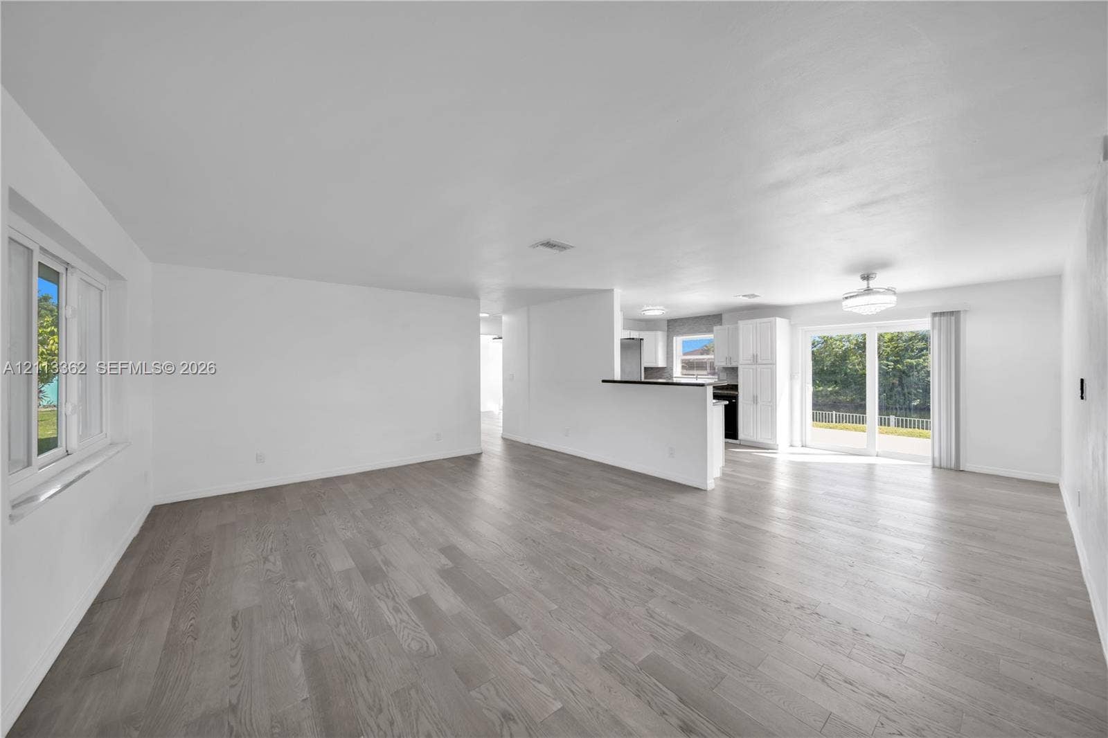 1206 NE 4th Terrace, Cape Coral, FL 33909 Open-concept area featuring wood-finish flooring, sliding glass doors, white cabinetry, a built-in counter, and neutral wall tones
