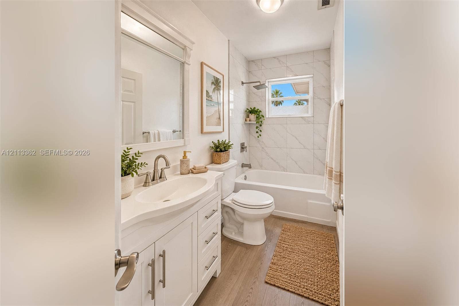 1206 NE 4th Terrace, Cape Coral, FL 33909 White vanity with integrated basin, polished metal hardware, framed mirror, light-toned wood-finish flooring, and tub-shower combination with floor-to-ceiling tile surround