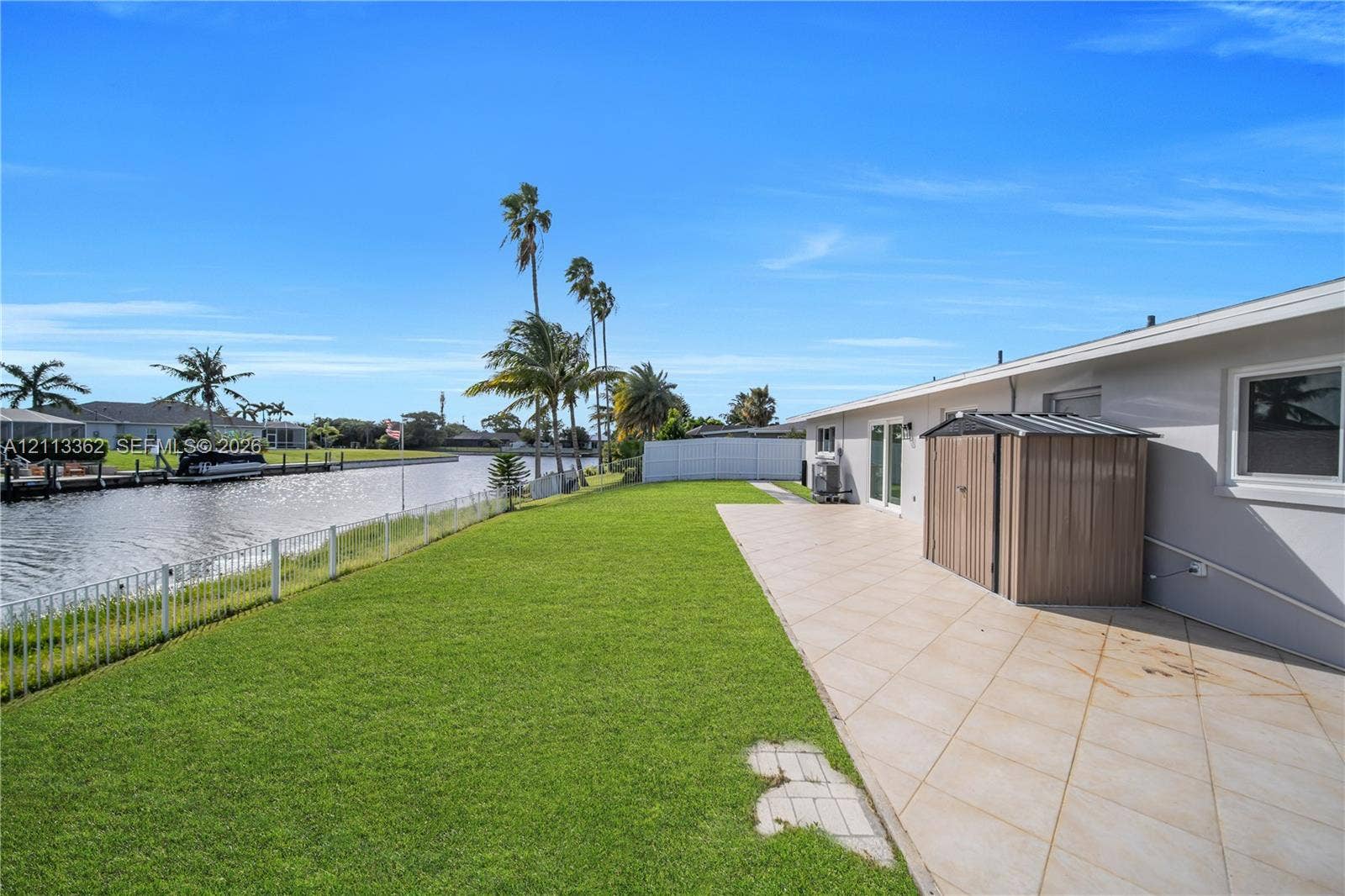 1206 NE 4th Terrace, Cape Coral, FL 33909 Waterfront backyard featuring a manicured lawn, tiled patio, and metal perimeter fencing
