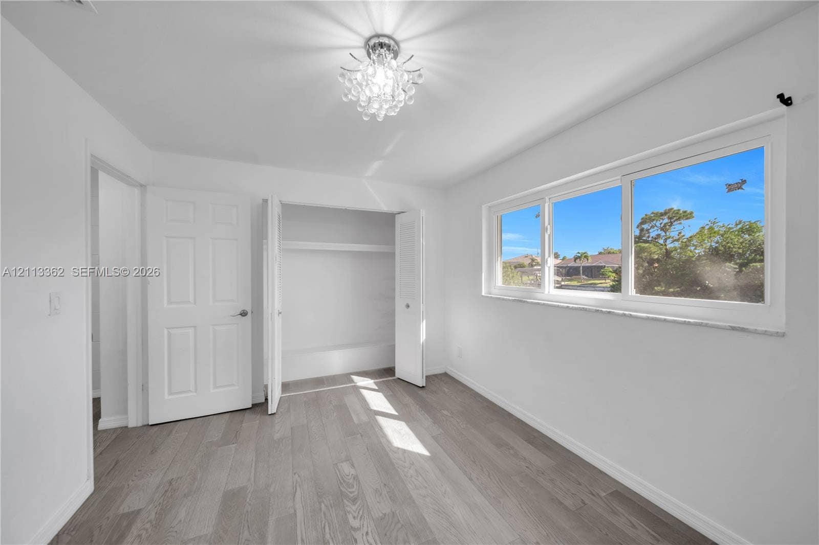1206 NE 4th Terrace, Cape Coral, FL 33909 Neutral-toned wood-finish flooring, crystal-style flush mount ceiling light, wide horizontal window with stone-finish sill, and double-door closet with built-in shelving