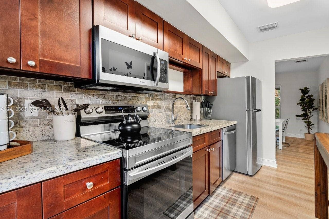 617 NE 9th Avenue, #72, Fort Lauderdale, Fort Lauderdale, FL 33304 Kitchen featuring stained wood cabinetry, stone-finish countertops, stainless steel appliances, and a tiled backsplash