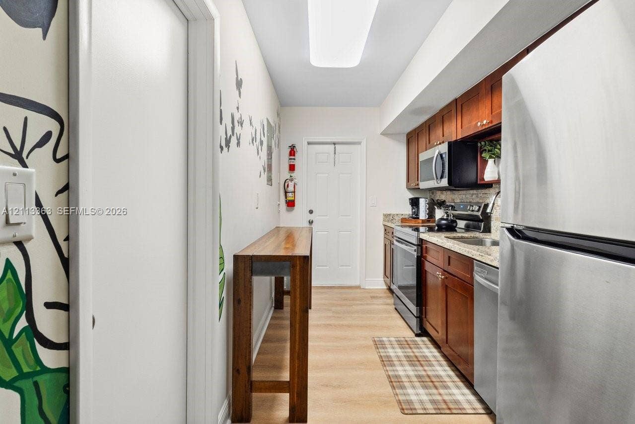 617 NE 9th Avenue, #72, Fort Lauderdale, Fort Lauderdale, FL 33304 Galley-style kitchen featuring wood cabinetry, stone-finish countertops, stainless steel appliances, and wood-finish flooring