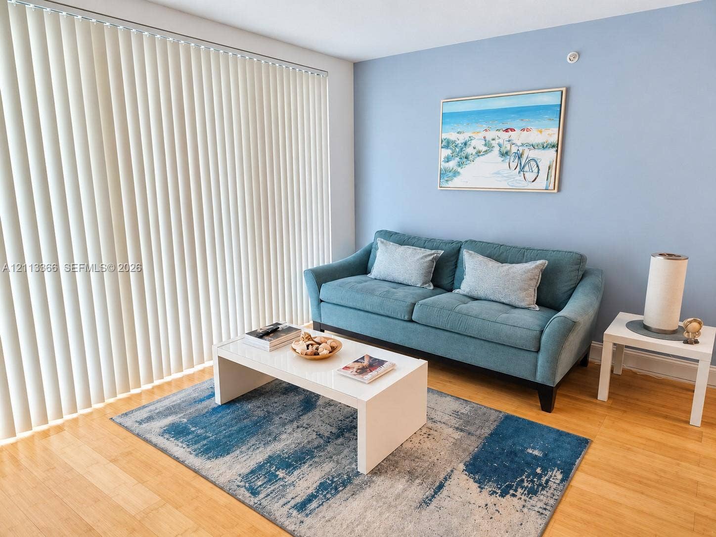 9499 Collins Avenue, #904, Surfside, FL 33154 Living area featuring wood-finish flooring, light blue painted walls, and vertical blinds