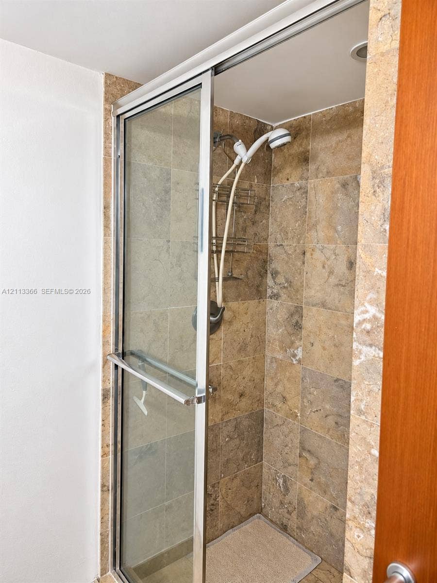 9499 Collins Avenue, #904, Surfside, FL 33154 Shower enclosure featuring natural stone wall tile, glass sliding door with chrome frame, and a hand-held shower fixture
