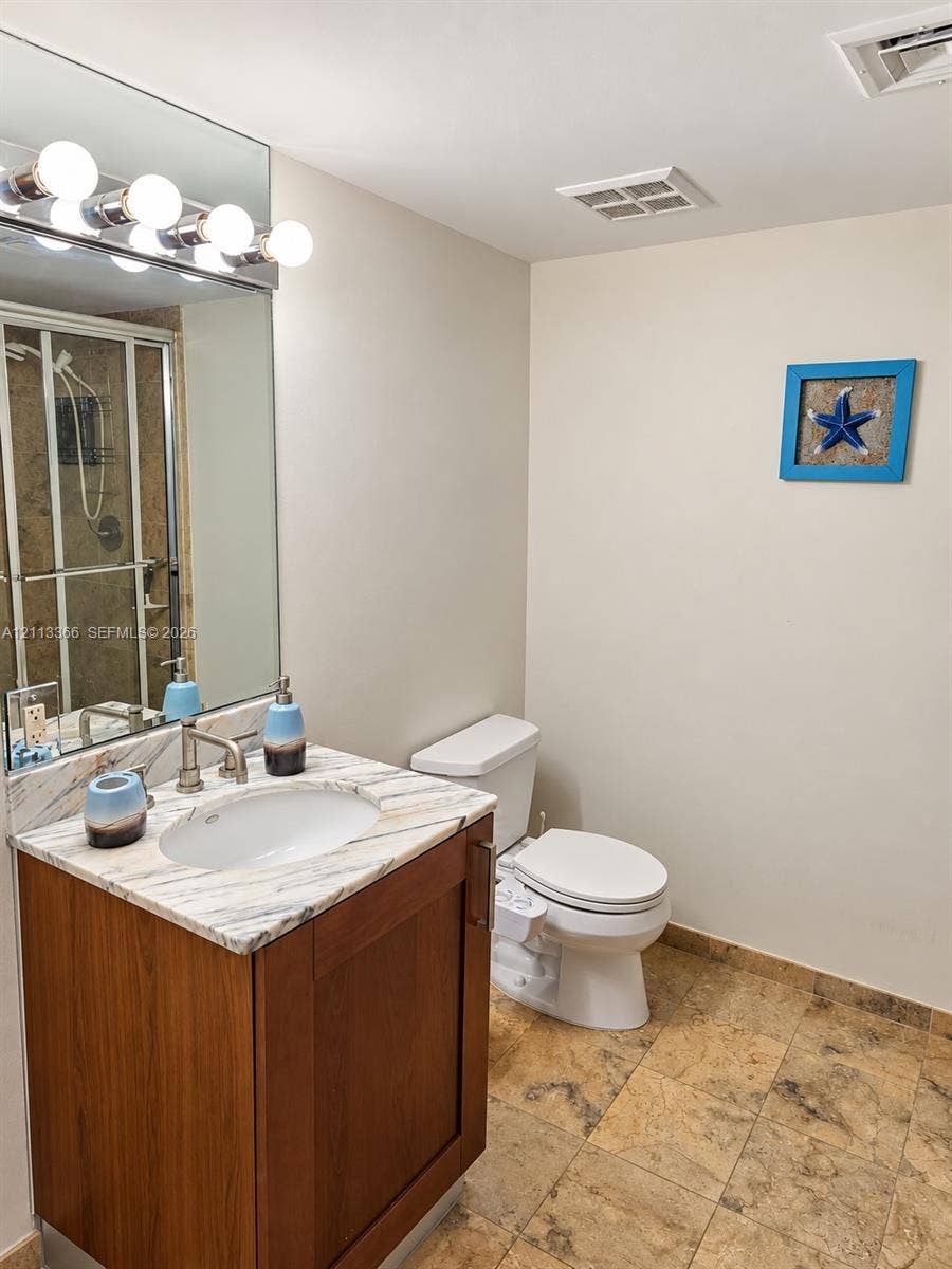 9499 Collins Avenue, #904, Surfside, FL 33154 Bathroom featuring a vanity with a light-veined countertop and an oval undermount sink, large wall-mounted mirror, brushed metal fixtures, and stone tile flooring