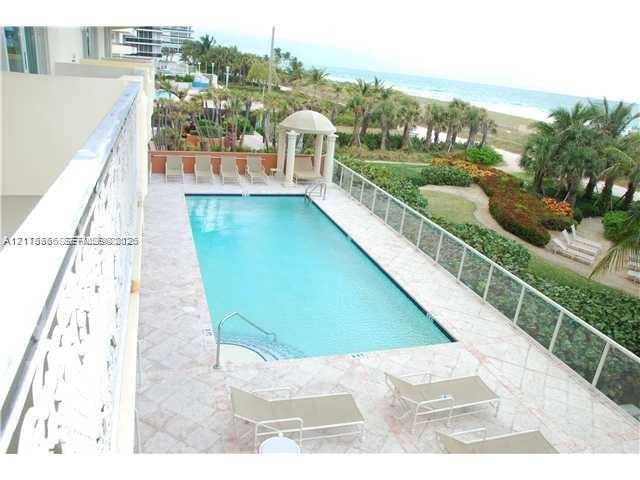 9499 Collins Avenue, #904, Surfside, FL 33154 Rectangular swimming pool featuring a tile deck, glass panel perimeter railing, and a columned cabana structure, situated against a sandy coastline backdrop