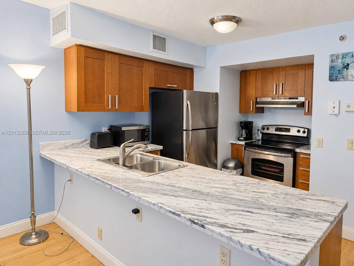 9499 Collins Avenue, #904, Surfside, FL 33154 Kitchen featuring wood-finish cabinetry, stone-patterned countertops, a stainless steel double-basin sink, and integrated stainless steel appliances