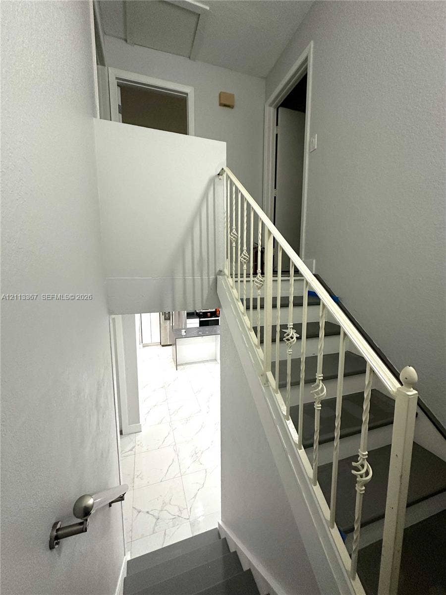 Staircase featuring dark-toned treads, decorative white metal balustrades, and a wall-mounted handrail