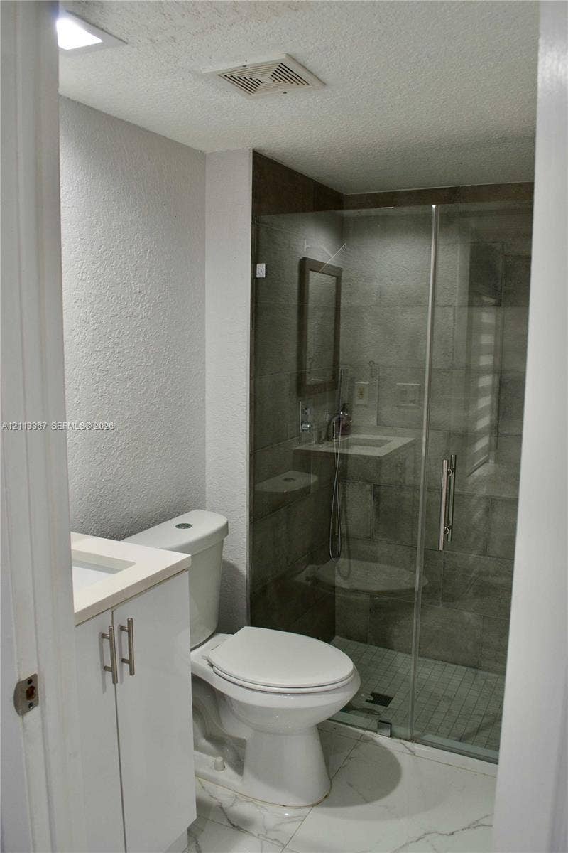 Bathroom featuring large-format tile flooring, white cabinetry with a light-toned countertop, and a walk-in shower enclosed by a glass door with tiled wall surrounds