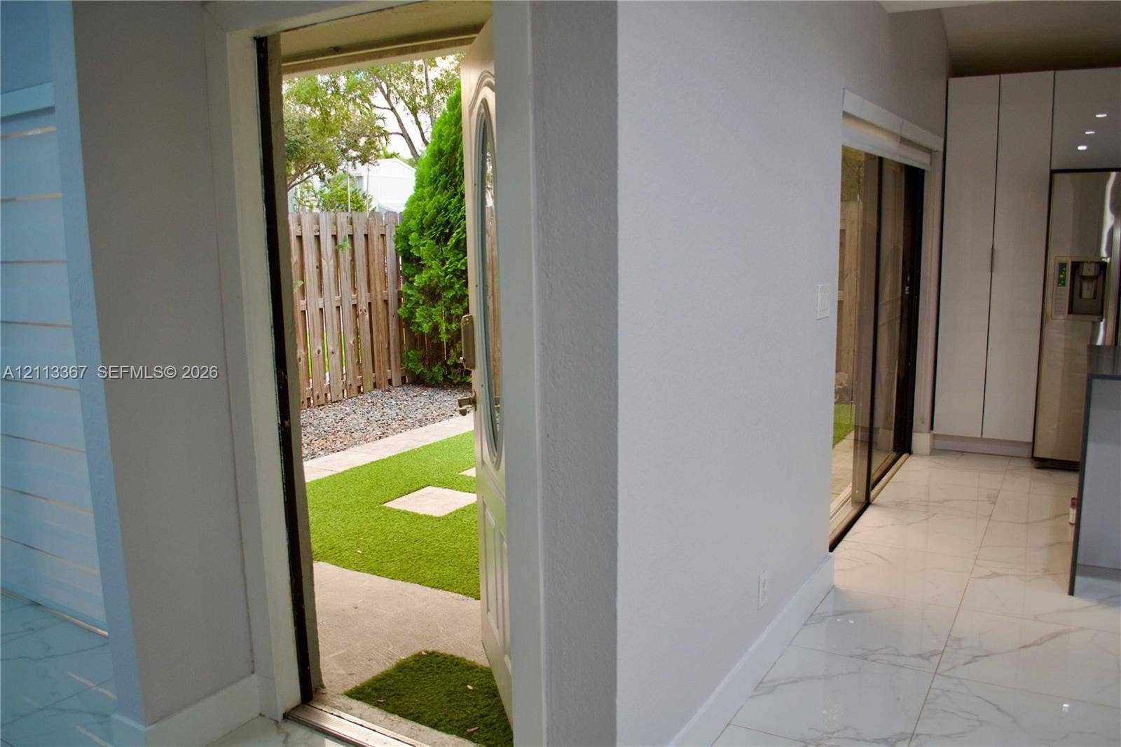 Large-format tile flooring, white floor-to-ceiling cabinetry, sliding glass door, and exterior access to a fenced courtyard featuring synthetic turf and stone pavers