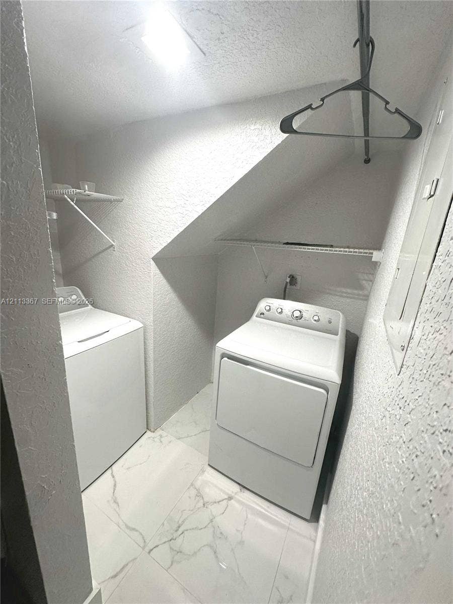 Utility space featuring white tile flooring with veining, overhead wire shelving, and recessed wall paneling