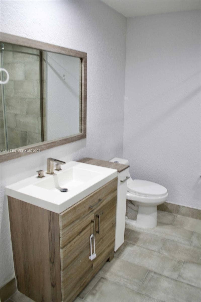Wood-finish vanity cabinet, integrated rectangular sink, wall-mounted mirror with a coordinating wood-finish frame, and tile flooring