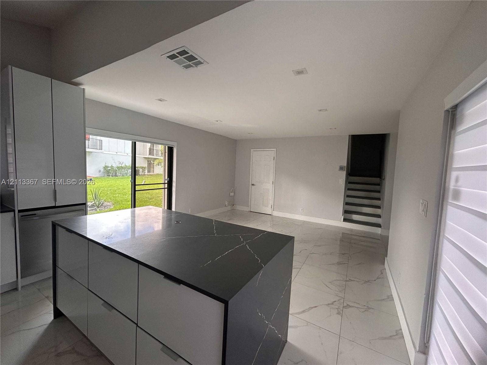 Kitchen featuring a waterfall-edge island with stone-finish countertop, white flat-panel cabinetry, large-format tile flooring, and sliding glass doors