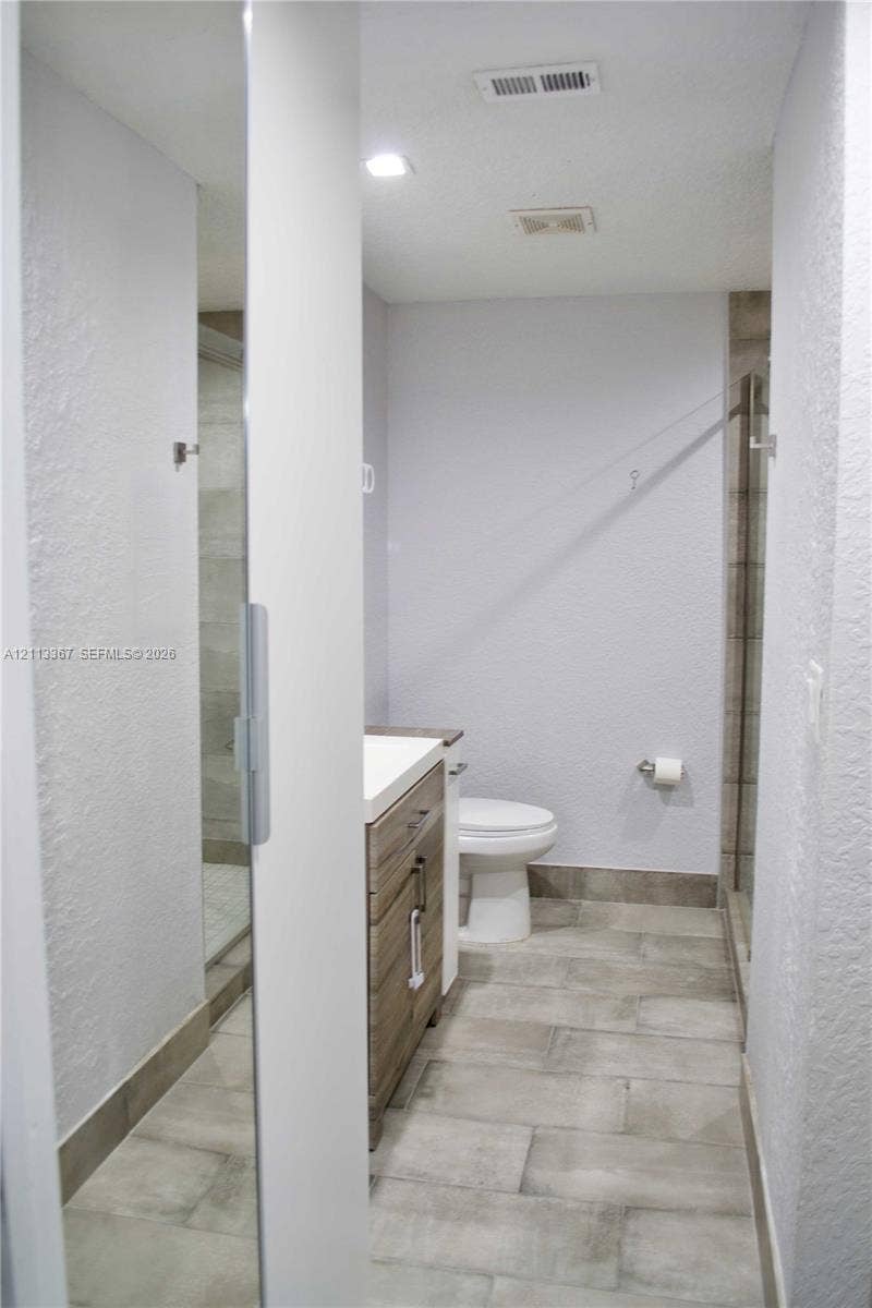 Bathroom featuring wood-finish vanity cabinetry, a rectangular sink, neutral large-format tile flooring, a glass-enclosed shower, and recessed ceiling lighting