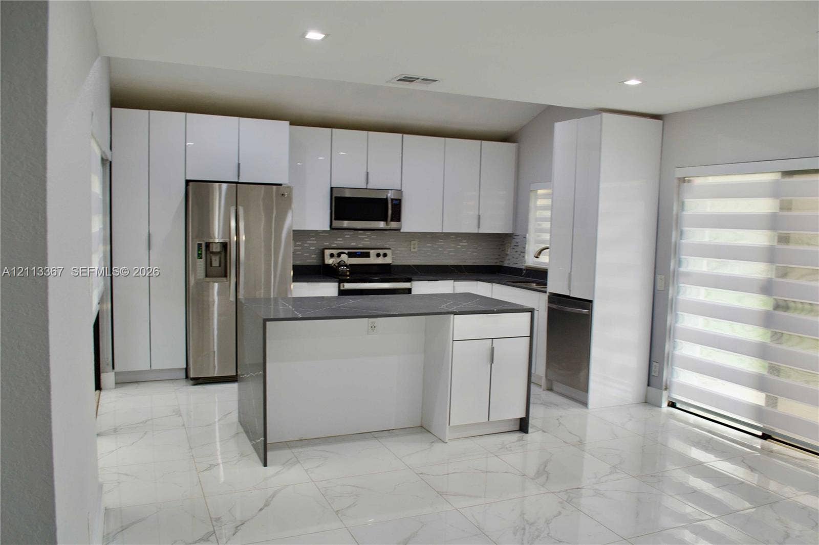 Kitchen featuring high-gloss white cabinetry, a center island with a dark stone countertop, stainless steel appliances, and large-format porcelain tile flooring