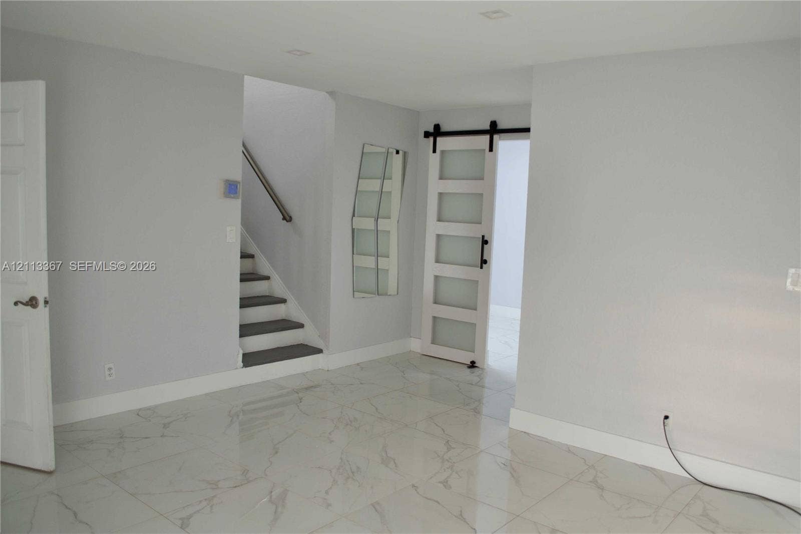 Interior space featuring polished stone-look tile flooring, a sliding barn-style door with frosted glass panels, recessed ceiling lighting, and a staircase with a handrail