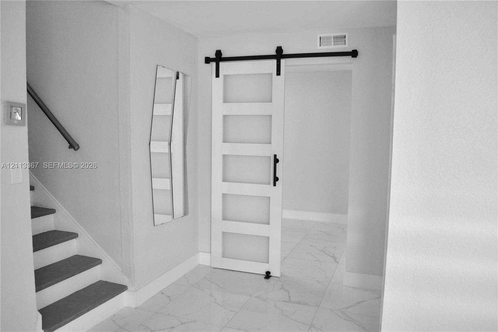 Interior featuring a white five-panel sliding barn door with frosted glass inserts, black iron hardware, stone-finish tile flooring with veining, and a staircase with a black handrail