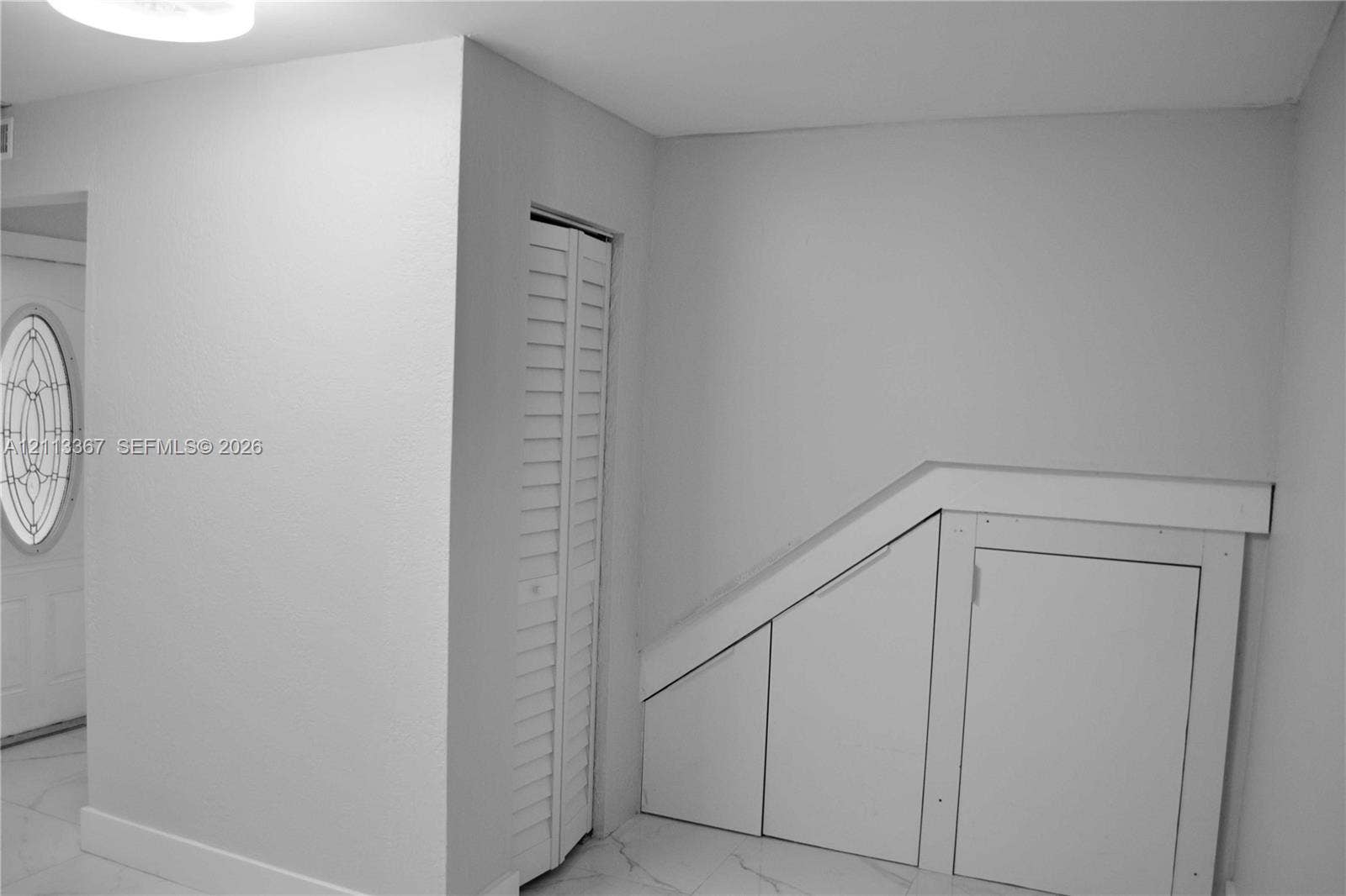 Entryway featuring white tile flooring, a louvered bi-fold closet door, and built-in under-stair storage cabinetry