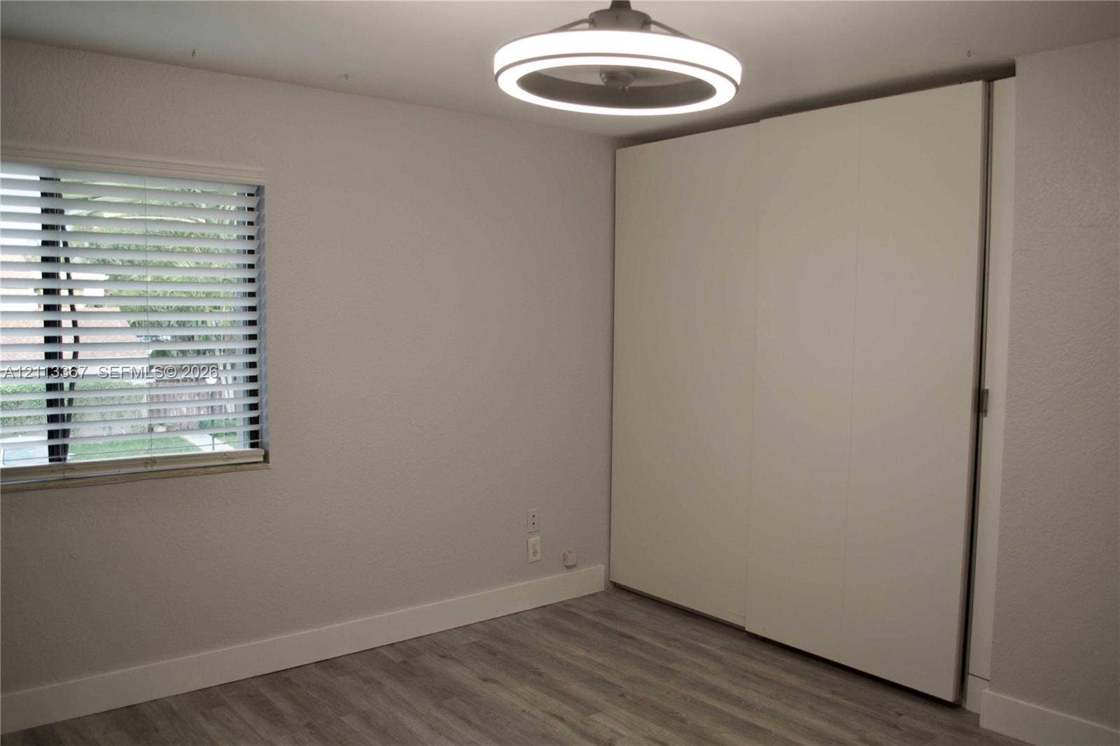 Room featuring wood-finish flooring, a wall-to-wall built-in closet with sliding doors, a horizontal-slat window blind, and a contemporary circular LED ceiling light fixture