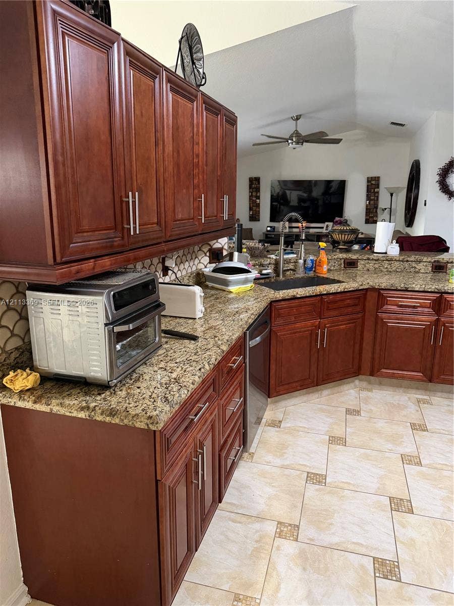 Kitchen featuring stained wood cabinetry, stone countertops, scalloped tile backsplash, integrated stainless steel appliances, and decorative tile flooring