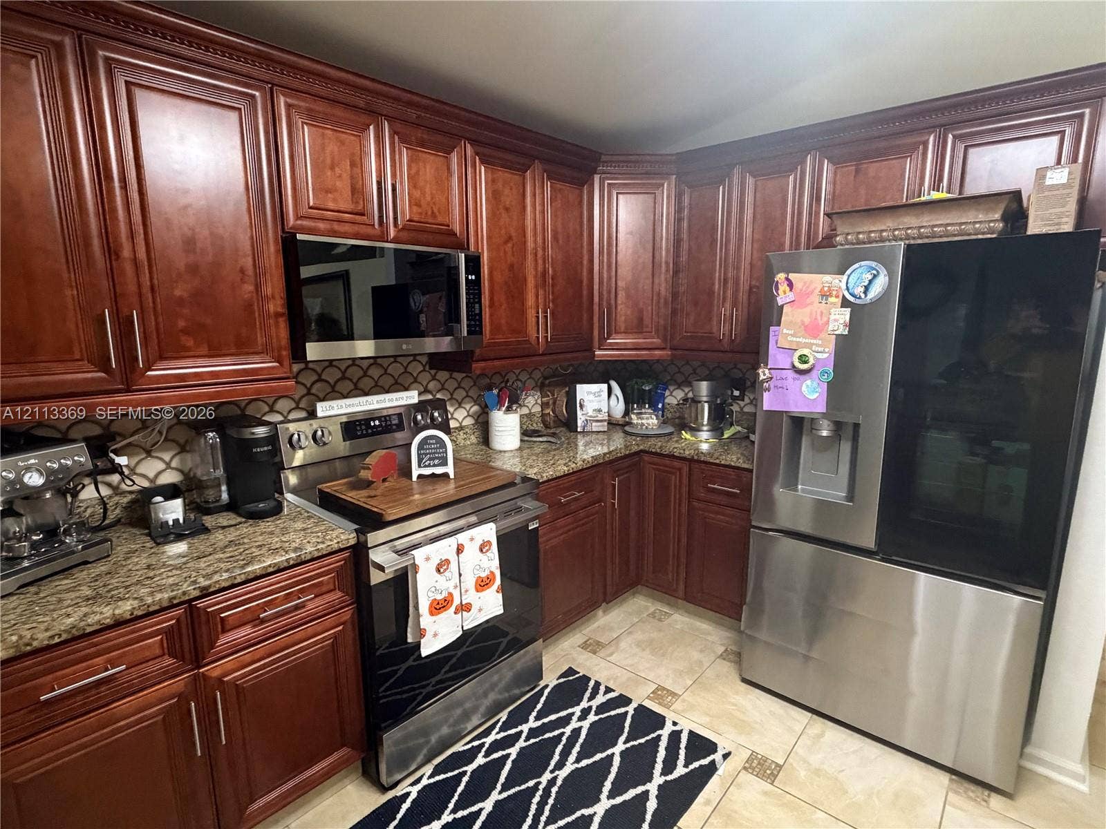 Rich wood cabinetry, stone countertops, stainless steel appliances, and decorative tile backsplash