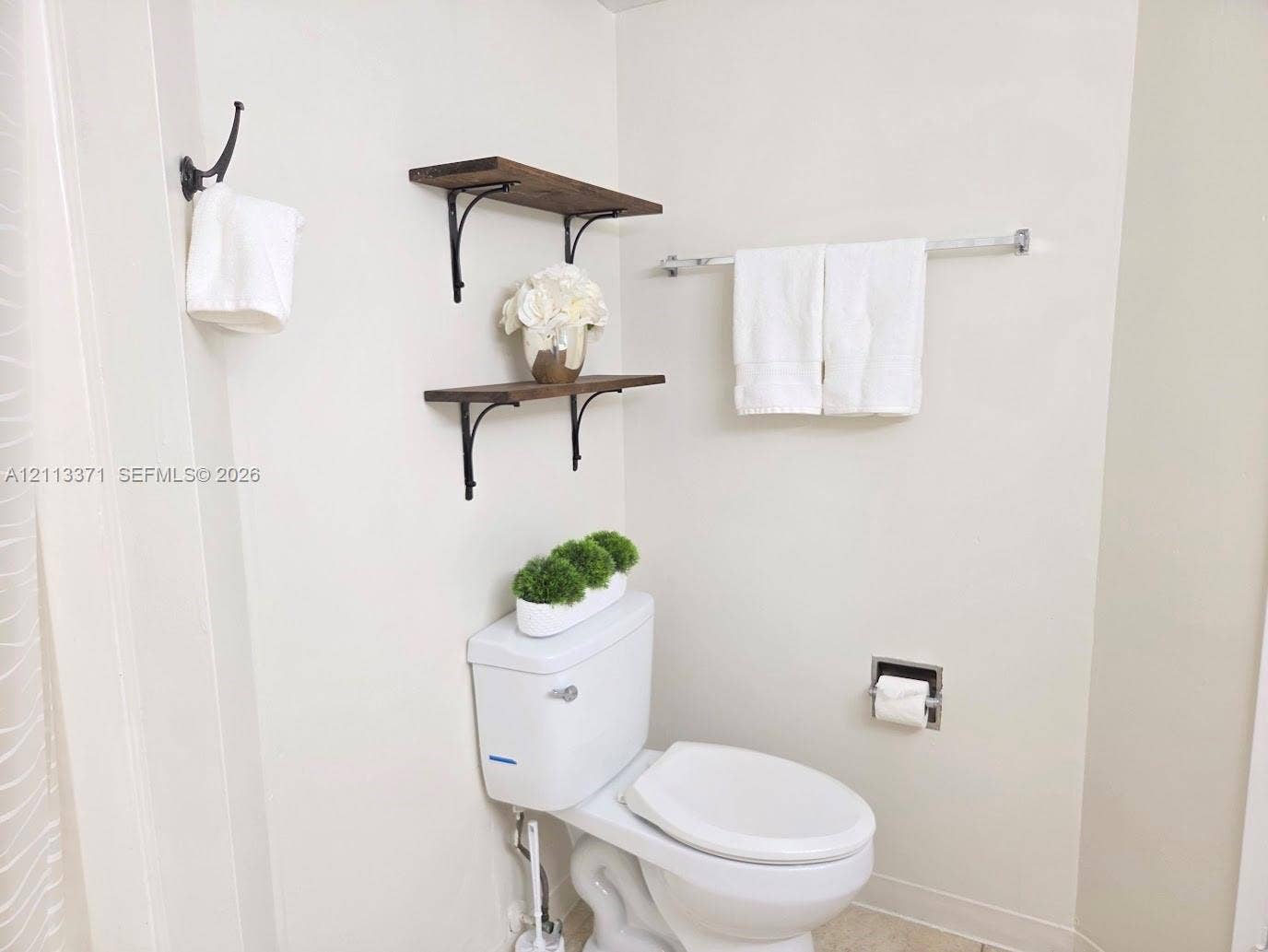9439 Fontainebleau Boulevard, #104, Miami, Miami, FL 33172 Wall-mounted wood-finish shelving with decorative metal brackets, chrome towel bar, and chrome recessed toilet paper holder