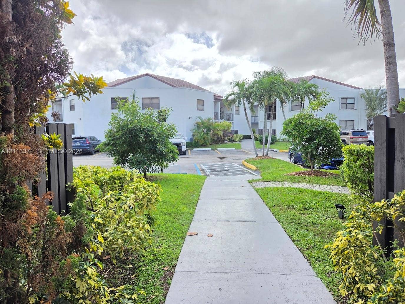 9439 Fontainebleau Boulevard, #104, Miami, Miami, FL 33172 Multi-story building exterior with a light-colored stucco facade and tile roof, concrete walkway, mature palm trees, and landscaped grounds