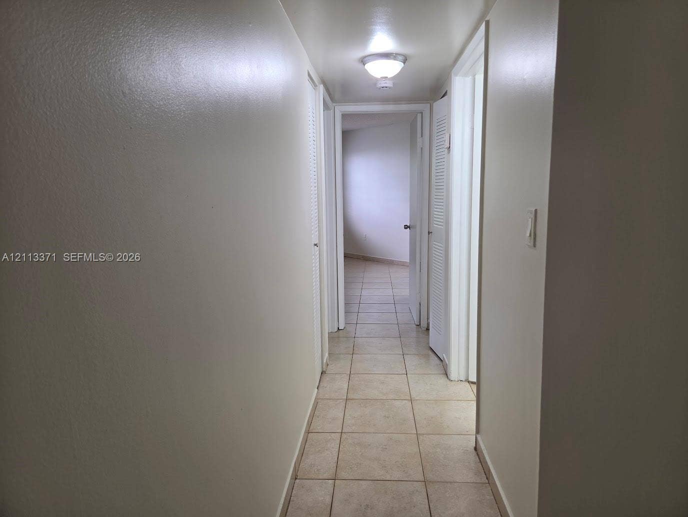 9439 Fontainebleau Boulevard, #104, Miami, Miami, FL 33172 Hallway featuring neutral wall finishes, tile flooring, louvered-panel closet doors, and a ceiling-mounted light fixture