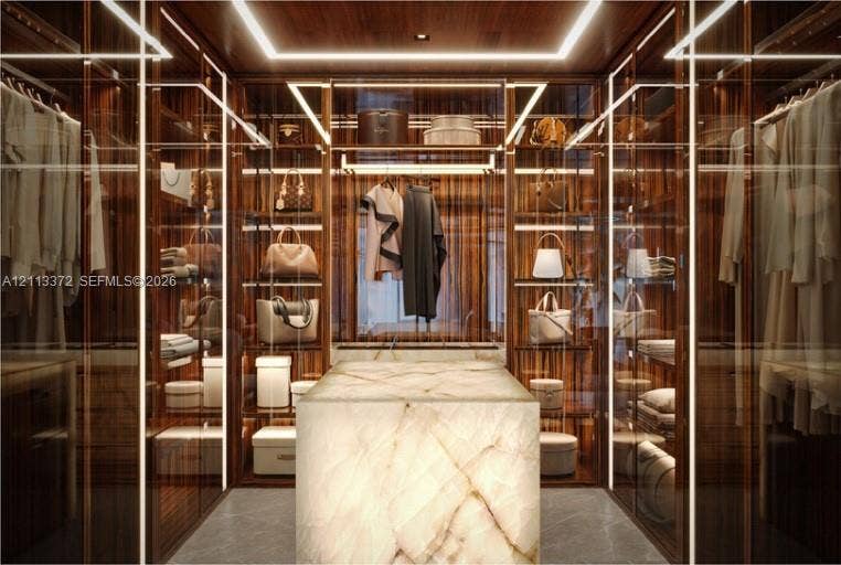 3312 NE 16th Court, Fort Lauderdale, FL 33305 Custom walk-in closet featuring floor-to-ceiling wood cabinetry, integrated linear LED lighting, glass-fronted storage displays, and a central stone island with a polished finish