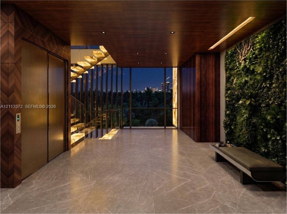 3312 NE 16th Court, Fort Lauderdale, FL 33305 Grand entrance hall featuring large-format stone flooring, a living plant wall, integrated metal elevator doors, wood-paneled ceilings with recessed lighting, and a floating staircase with glass railings
