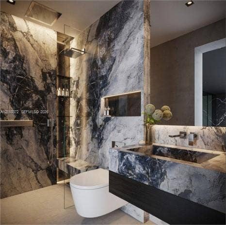 3312 NE 16th Court, Fort Lauderdale, FL 33305 Bathroom featuring large-format stone wall cladding, floating vanity with integrated stone sink, wall-mounted faucet, recessed shelf with accent lighting, and a glass-enclosed shower with a rainfall showerhead