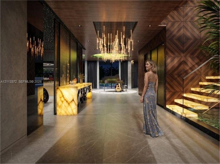 3312 NE 16th Court, Fort Lauderdale, FL 33305 Foyer featuring large-format stone-finish floor tile, geometric wood-paneled walls, custom illuminated stone console, tiered linear chandelier, and floating staircase with backlit treads