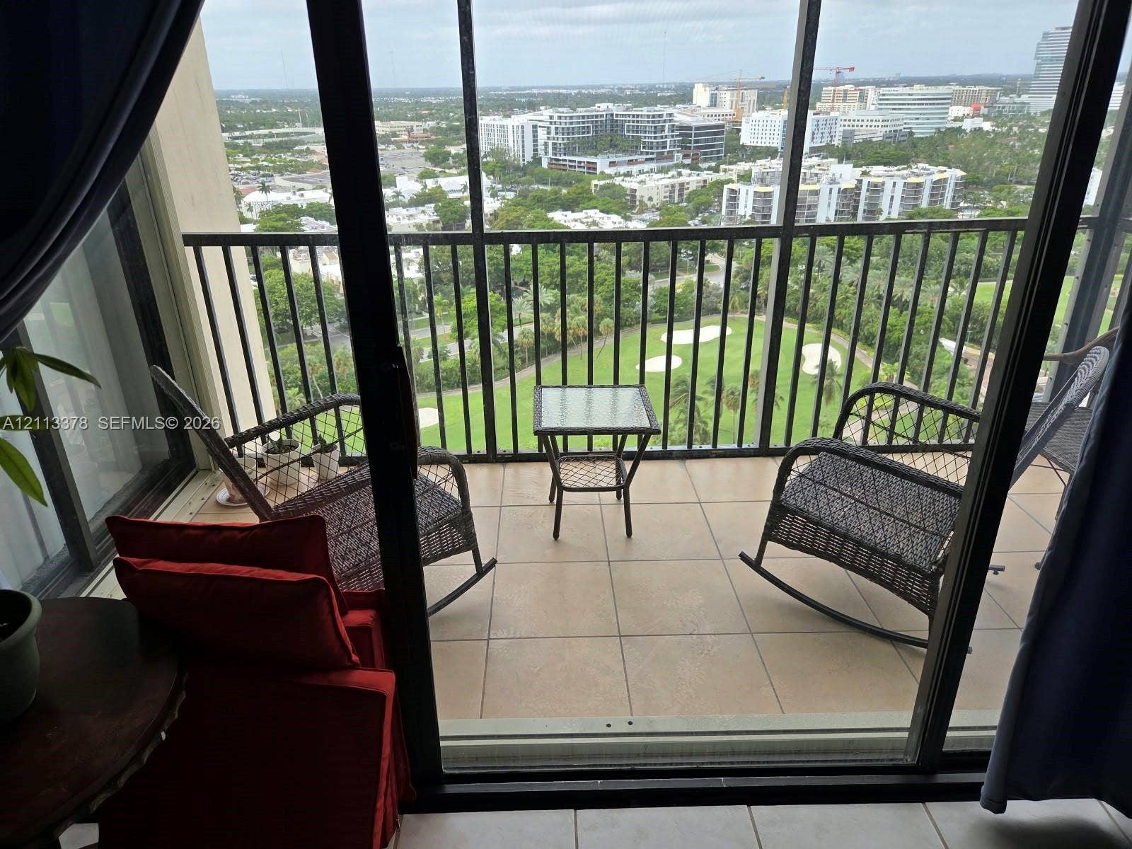 20335 W Country Club Drive, #2302, Aventura, FL 33180 Screened balcony featuring tiled flooring and black metal railings, overlooking a landscaped green space and urban skyline