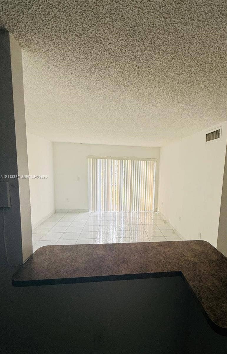 15610 SW 80th Street, #J-103, Miami, FL 33193 L-shaped countertop with a dark finish, white tile flooring, and vertical blinds covering a large sliding glass door