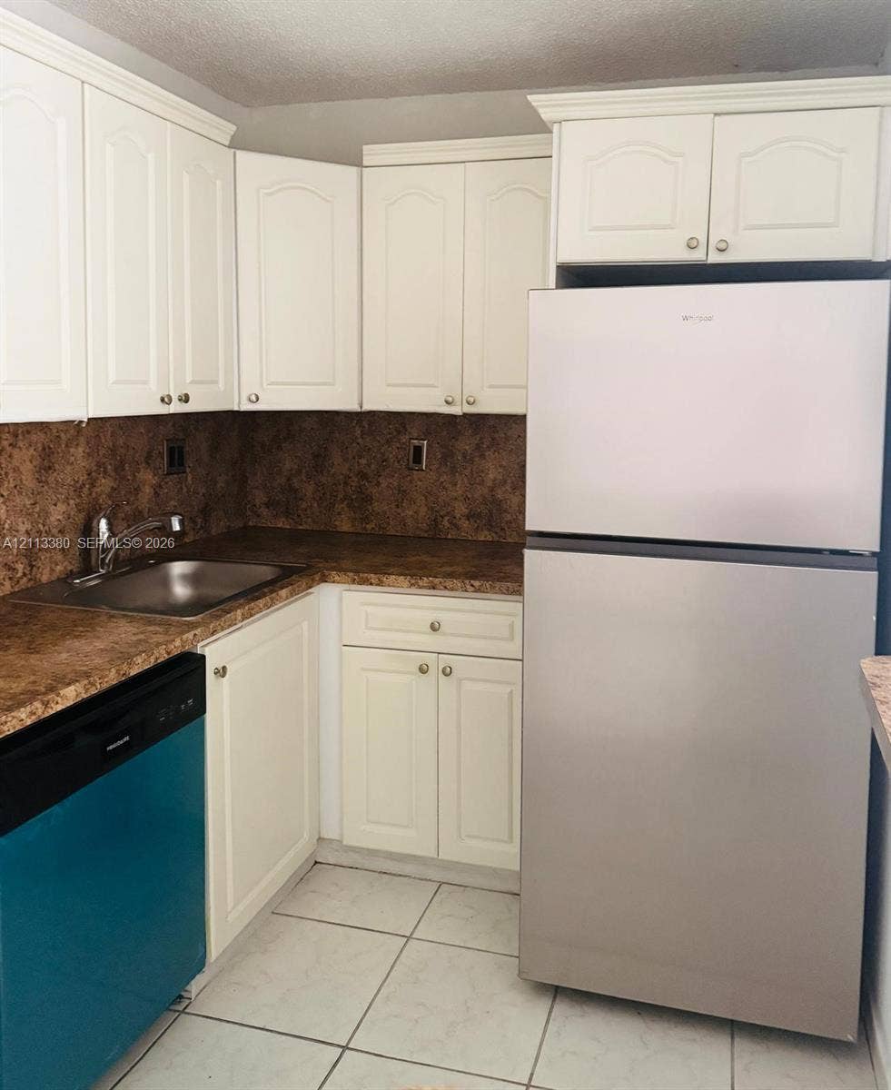 15610 SW 80th Street, #J-103, Miami, FL 33193 Kitchen featuring white shaker-style cabinetry, a stainless steel refrigerator, patterned laminate countertops, a stainless steel sink with a high-arch faucet, and ceramic tile flooring