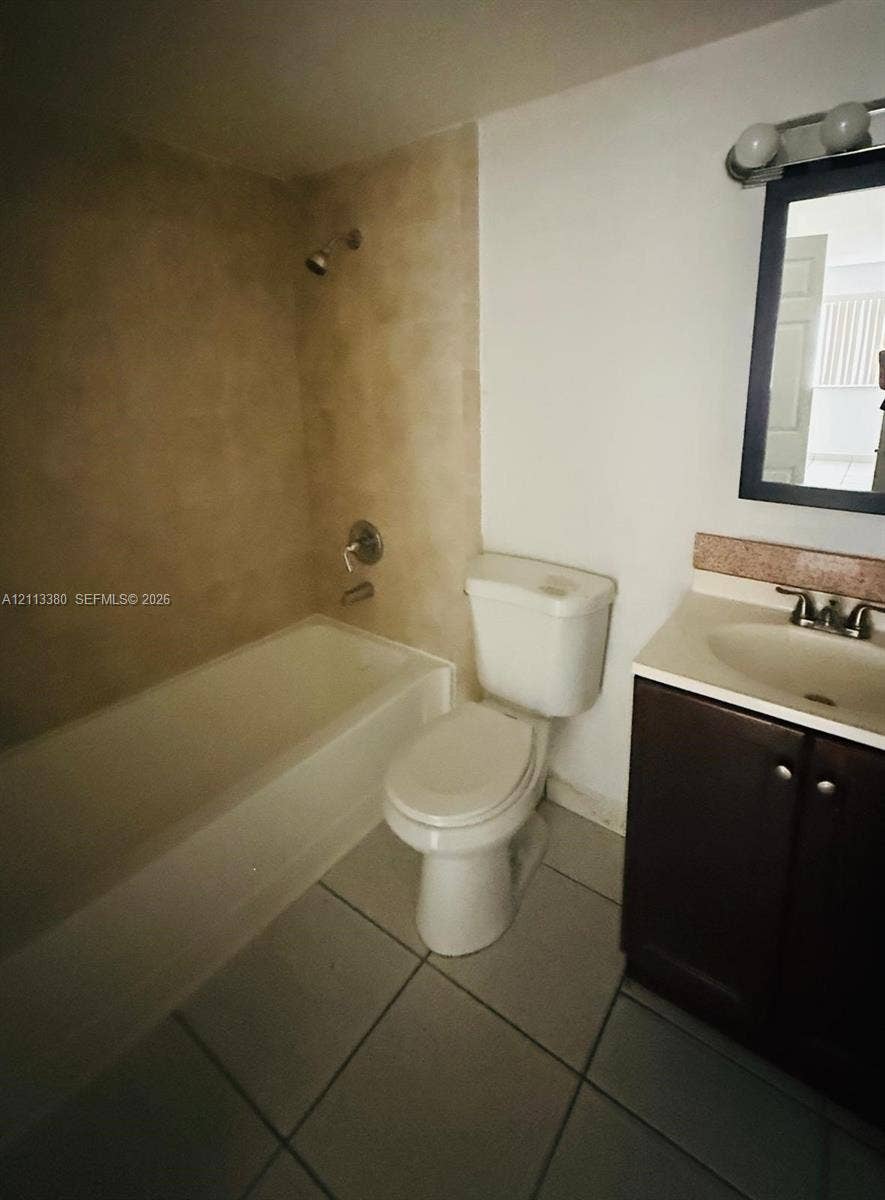 15610 SW 80th Street, #J-103, Miami, FL 33193 Full bathroom featuring a tub-shower combination with tile surround, a dark-finish wood vanity with a solid surface countertop, ceramic tile flooring, and a framed wall-mounted mirror