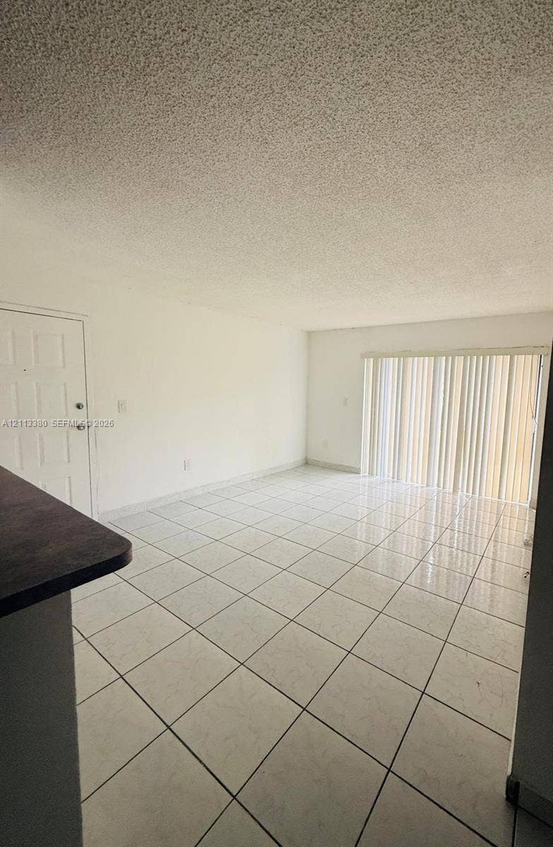 15610 SW 80th Street, #J-103, Miami, FL 33193 Interior space featuring large-format ceramic tile flooring, a six-panel entry door, and vertical blind window treatments