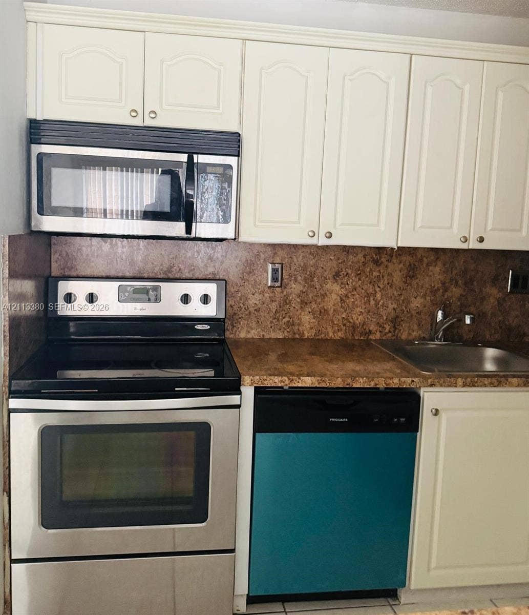 15610 SW 80th Street, #J-103, Miami, FL 33193 Kitchen featuring off-white raised-panel cabinetry, stone-finish countertops, stainless steel electric range, over-the-range microwave, and stainless steel undermount sink